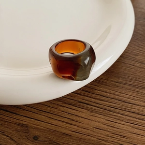 Detailed close-up of amber colored resin ring on a white ceramic plate and wooden background