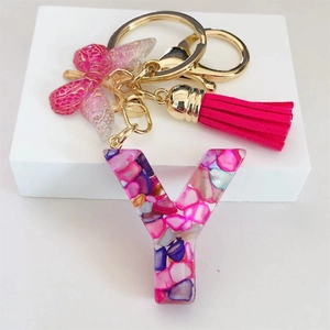 Detail of pink resin letter Y keychain with shell flakes, butterfly charm and silk tassel