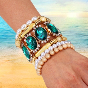 Detail view of emerald crystal and pearl layered bracelets worn on a beach setting