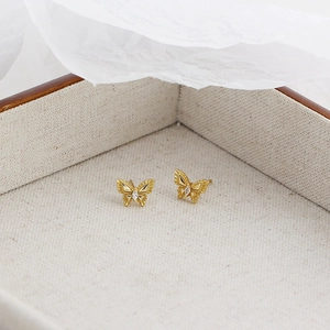 Détail macro de boucles d'oreilles papillon dorées avec cristaux dans une boîte en lin
