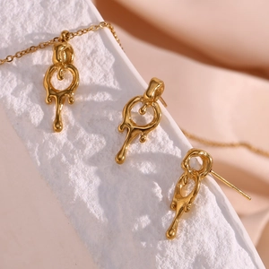Detail of 18K gold plated lava-style fluid earrings and necklace pendant set on stone