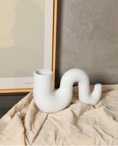 Vue détaillée d'un vase en céramique blanc mat en forme de S sur un tissu en lin