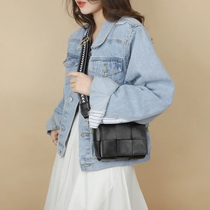 Detailed view of black woven leather crossbody bag with ethnic patterned wide strap