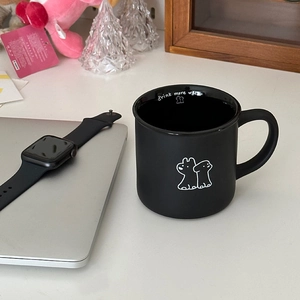 Detail of black ceramic mug featuring drink more water text and white dog illustration