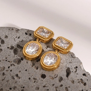 Macro detail of gold-plated earrings with clear rectangular and oval zircons on rock