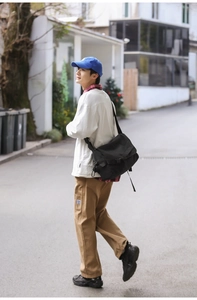 Street style shot of a man wearing a large black canvas messenger bag outdoors