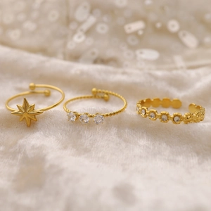 Detail of three gold plated adjustable rings with star and zircon on soft beige fabric