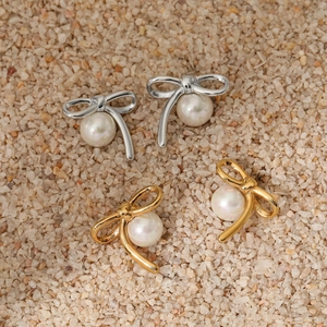 Orecchini asimmetrici con fiocco e perla in oro e argento su fondo di sabbia ruvida