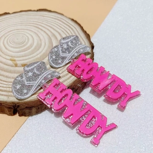 Detail of silver glitter cowboy hat earrings with pink HOWDY text on a wooden base