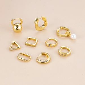 Set of gold geometric hoop earrings with pearls and zircons on beige background