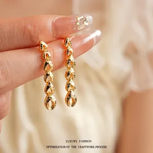 Elegant gold tassel earrings with hollow water-drop links shown on a soft fabric background