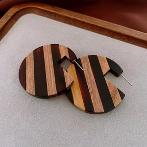 Detailed close-up of C-shaped hoop earrings featuring striped resin and wood textures