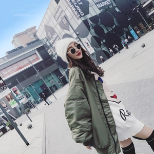 Women's white knitted beanie paired with an oversized green bomber jacket in urban setting