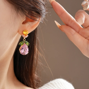 Macro shot of colorful zircon drop earrings with pink gemstone and green leaf accents
