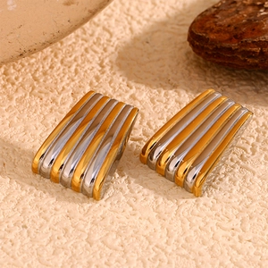 Détails macro des boucles d'oreilles trapèze rayées dorées et argentées sur texture pierre