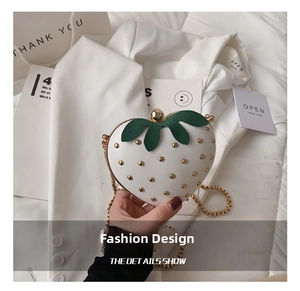 Close-up of strawberry-shaped handbag with golden studs and chain strap
