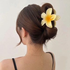 Detailed view of a gradient yellow plumeria hair claw clip securing a low bun hairstyle