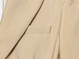 Detail van champagnegouden blazer met nauwkeurige revers-snit en borstzaktextuur op stof