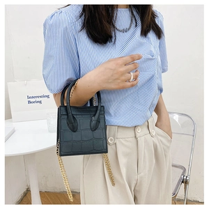 Detail of black crocodile texture mini bag with golden chain strap on a stylish model