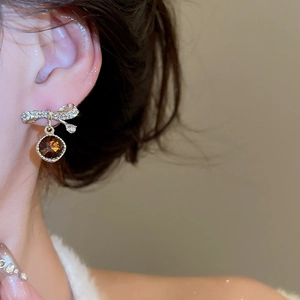 Close-up of bow earrings with sparkling rhinestones and amber round gemstone drop