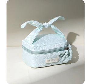 Detail view of light blue jacquard cosmetic bag with floral embroidery and bow handle