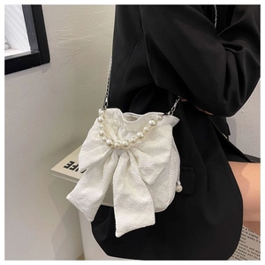 Detail of white bow-shaped bag featuring pearl handle and jacquard fabric texture on a model