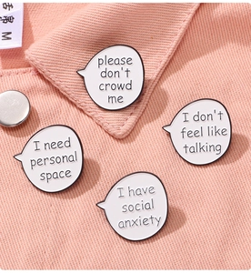 Detail of four white enamel brooches with social anxiety quotes on a pink shirt collar