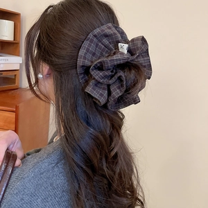 Detail of a dark plaid double-layered scrunchie worn by a model in a minimalist setting