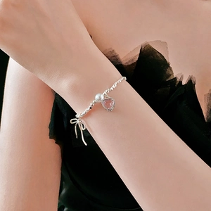 Close-up of beaded silver bracelet featuring a pink heart gem and bow charms on wrist