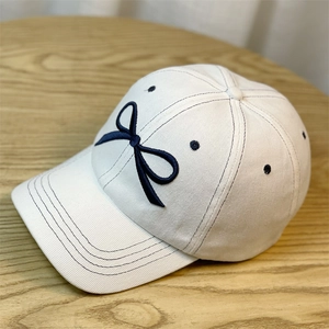 Detail shot of navy blue bow embroidery on a white cotton baseball cap over wood surface