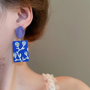 Detail shot of vintage painted flower drop earrings on a model showing purple petal design