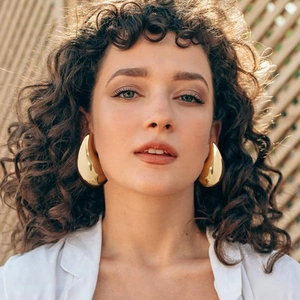 Detailed view of large gold teardrop earrings worn by a model in natural outdoor sunlight