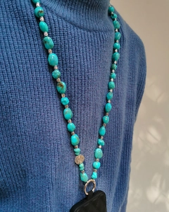 Detail of bohemian turquoise beaded phone strap with silver charm on blue sweater