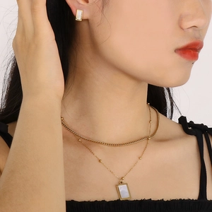 Macro detail of gold layered necklace with rectangular shell pendant and matching stud earrings