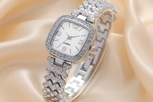 Macro detail of a silver square quartz watch with rhinestones on champagne silk fabric