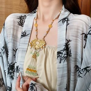 Close-up of gold pendant necklace with pearls and green jade tassels on a model