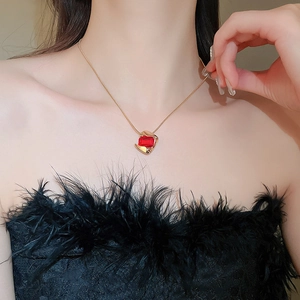 Close-up of a gold geometric necklace with a red rectangular gemstone on a model