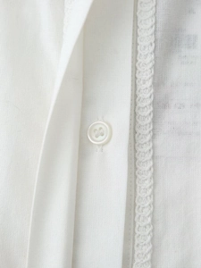 Vue détaillée d'une chemise en coton et lin blanc avec bordure en dentelle et bouton rond