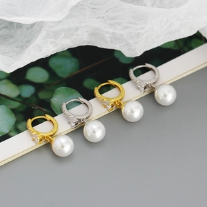 Close-up of gold and silver pearl earrings with zircon inlay on a textured white surface