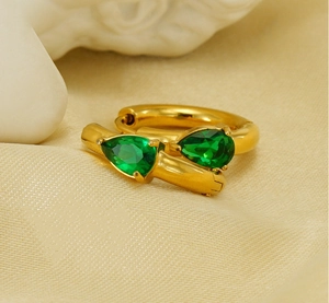 Detail of gold snake earrings featuring pear-cut green emerald stones on silk fabric