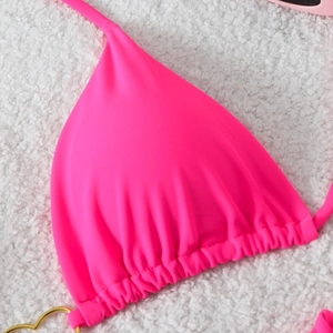 Detail of neon pink bikini top with triangle cups and gold heart-shaped metal ring