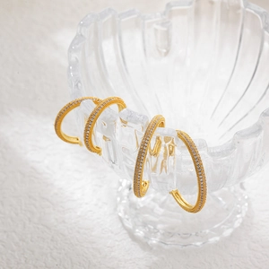 Macro shot of gold hoop earrings with micro-pave cubic zirconia on a textured glass base