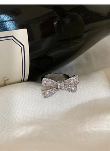 Macro shot of silver bow ring with zircon pavé setting on white textured fabric
