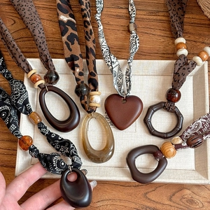 Ethnic fabric necklace collection with wood and acrylic pendants on a wooden background