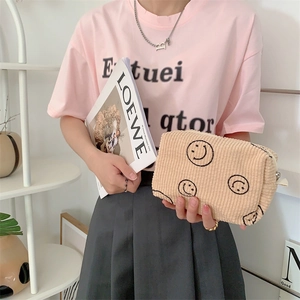 Detail of beige corduroy makeup bag featuring black smiley face embroidery and zip top