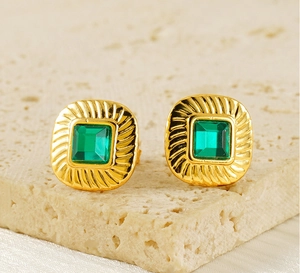 Macro shot of vintage gold square earrings with green zircon inlay on stone surface