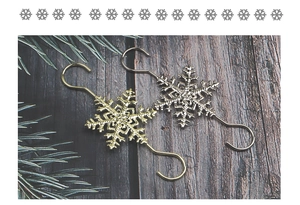 Close-up of gold and silver snowflake S-hooks on dark wood with festive pine branches