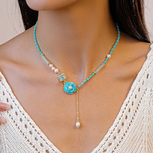 Detail of beaded necklace featuring blue enamel flower, pearls, and a crystal pendant