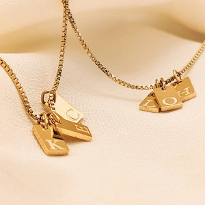 Detailed close-up of gold-plated box chain and rectangular alphabet charms on beige fabric
