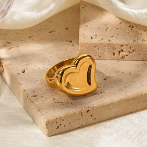 Detailed view of polished 18K gold heart ring on textured stone and cream silk background
